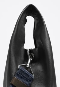 Črna usnjena torbica z gladko teksturo, edinstvenim odprtjem v obliki luknje, srebrnimi dodatki in akcentnim trakom v mornarsko modri barvi.