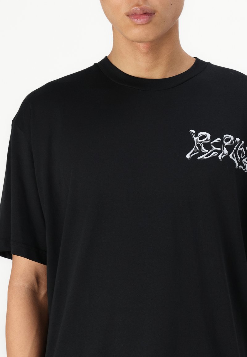 Camiseta de algodón negra con un ajuste relajado, con un diseño gráfico texturizado en blanco en el lado izquierdo del pecho, tejido suave y mangas cortas.