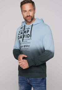Sudadera con capucha en un degradado de azul a verde, con texto y detalles en negro. Tejido suave, puños de canalé y cordones de capucha texturizados.