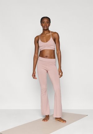 Ανοιχτό ροζ αθλητικό σουτιέν και φαρδιές παντελόνες γιόγκα από απαλό, ελαστικό ύφασμα, με ρυτιδιασμένη λεπτομέρεια στο σουτιέν και λεία μέση.