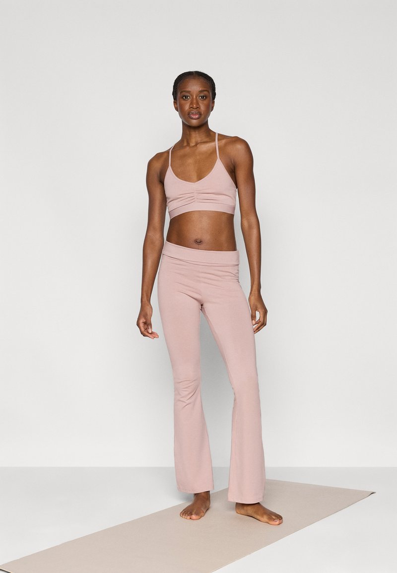 Ανοιχτό ροζ αθλητικό σουτιέν και φαρδιές παντελόνες γιόγκα από απαλό, ελαστικό ύφασμα, με ρυτιδιασμένη λεπτομέρεια στο σουτιέν και λεία μέση.