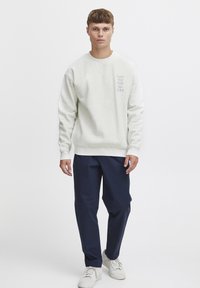 Felpa in cotone grigia chiara con collo rotondo e stampa di testo, abbinata a pantaloni blu navy e sneakers bianche. Vestibilità semplice e rilassata.