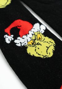 Calze nere con una grafica gialla del Grinch che indossa un cappello di Babbo Natale rosso e bianco, con un motivo a maglia testurizzato e un contrasto di colori vivaci.