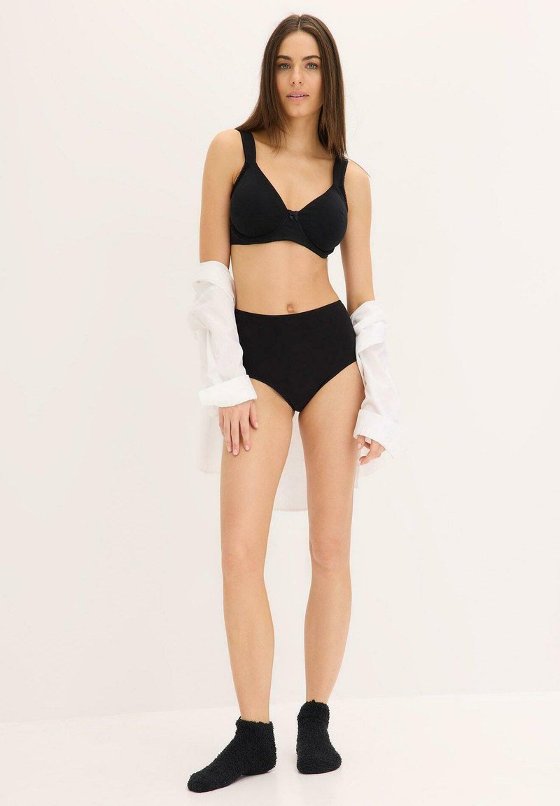 Reggiseno nero e pantaloni alti in vita realizzati in tessuto liscio, indossati con una camicia bianca. La modella indossa calzini neri pelosi alla caviglia.