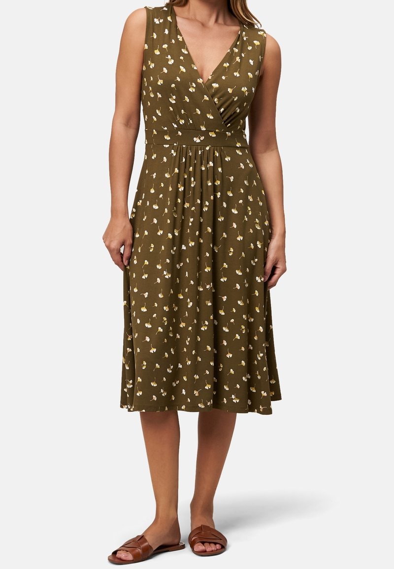 Robe midi sans manches vert olive avec un petit imprimé floral jaune et blanc, corsage cache-cœur col en V, jupe plissée, portée avec des sandales plates marron.