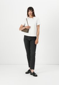 Witte t-shirt met korte mouwen, aansluitend ontwerp, gecombineerd met donkere spijkerbroek. Model draagt een kleine bruine handtas en heeft zwarte instappers aan.