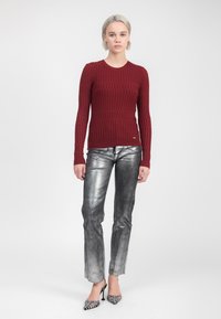Rode geribbelde trui met lange mouwen, gecombineerd met glanzende zilveren rechte broek en zwart-wit gestreepte hakken. Minimalistische achtergrond.