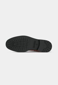 Brown leather shoe with a prominent black rubber sole. The sole features a detailed tread pattern for traction and durability.