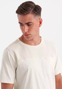 Lysecreme kortærmet t-shirt med et tekstureret øverste panel og en lille lomme detalje. Blødt stof med en afslappet pasform.