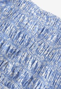 Helle blaue Stoff mit floralem Muster. Verfügt über geraffte Textur und horizontale Falten, die Dehnbarkeit und Struktur verleihen.