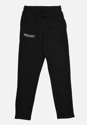 Zwarte joggingbroek met elastische tailleband en trekkoord, met witte tekst op de linker dij met de tekst "There is beauty in simplicity..."