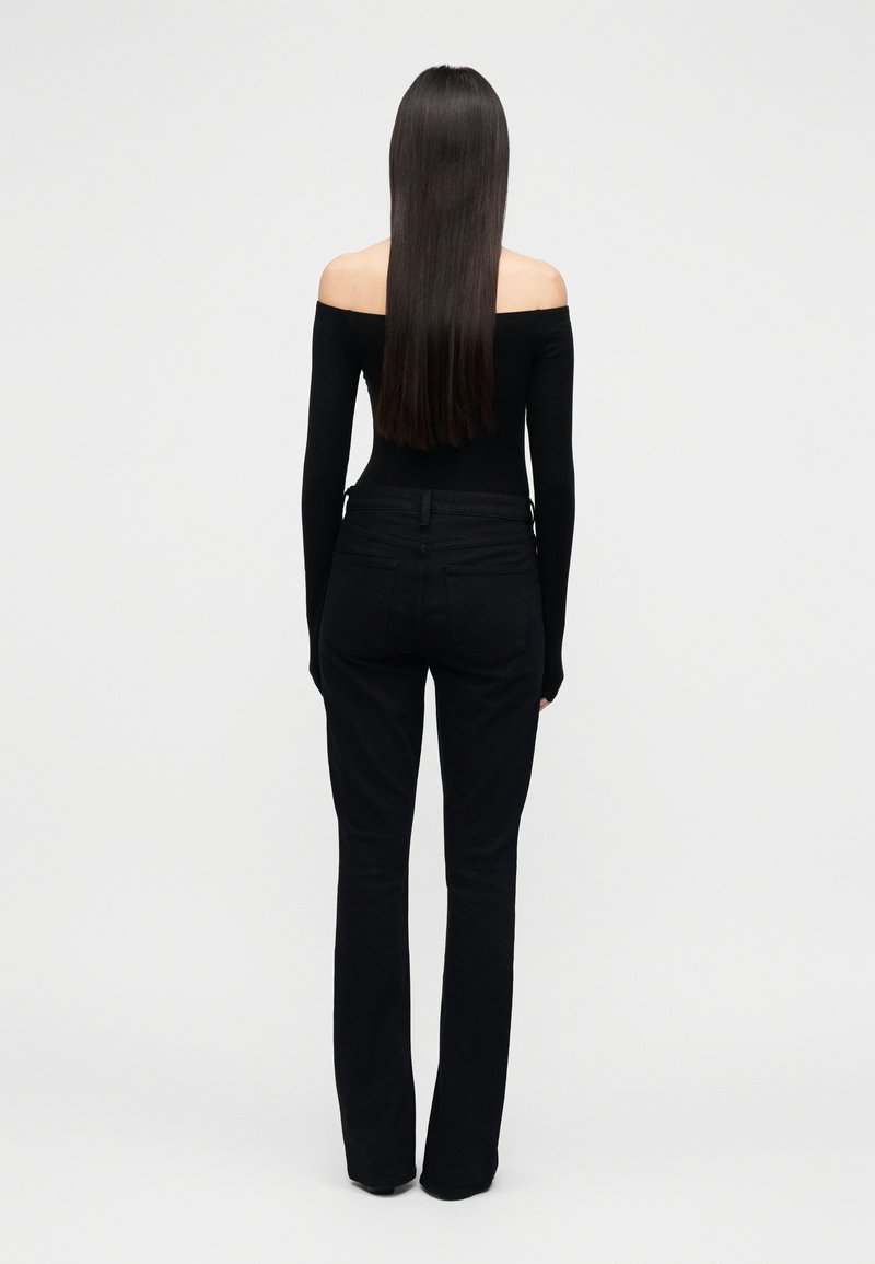 Haut noir à épaules dénudées associé à un jean noir ajusté. Tissu lisse, silhouette près du corps, et poches arrière discrètes. Modèle vu de dos.