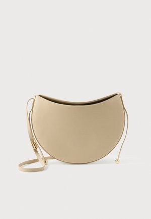 Sac d'épaule beige en forme de croissant avec une fine sangle réglable et des perles dorées aux extrémités du cordon.