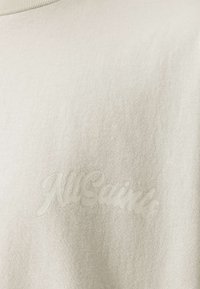 Μπεζ βαμβακερό t-shirt σε ανοιχτή απόχρωση με διακριτικό ανάγλυφο λογότυπο "AllSaints". Το ύφασμα έχει λεία υφή και κλασικό στρογγυλό λαιμό.