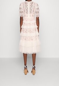 Bílé vrstvené šaty s květinovou výšivkou, průsvitným materiálem a volánovými rukávy. Styl doplňují korkové sandály na podpatku s vázáním kolem kotníků.