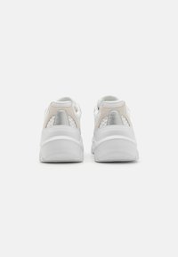 White sneakers with pink and silver accents, mesh material, rounded shape, and thick soles. Soft texture with padded collar and heel.
