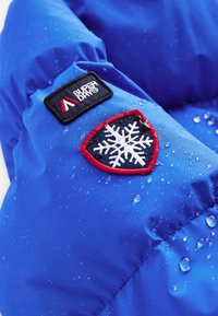 Hele sinine puffer-jaki materjal läikiva tekstuuriga, millel on punaste ja valgete detailidega lumekuhja plaastriga ning pinnal veepiisad.