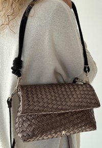 Sac à main en bronze métallique tissé avec un design plié, doté d'une sangle noire tressée et d'accessoires en métal argenté.