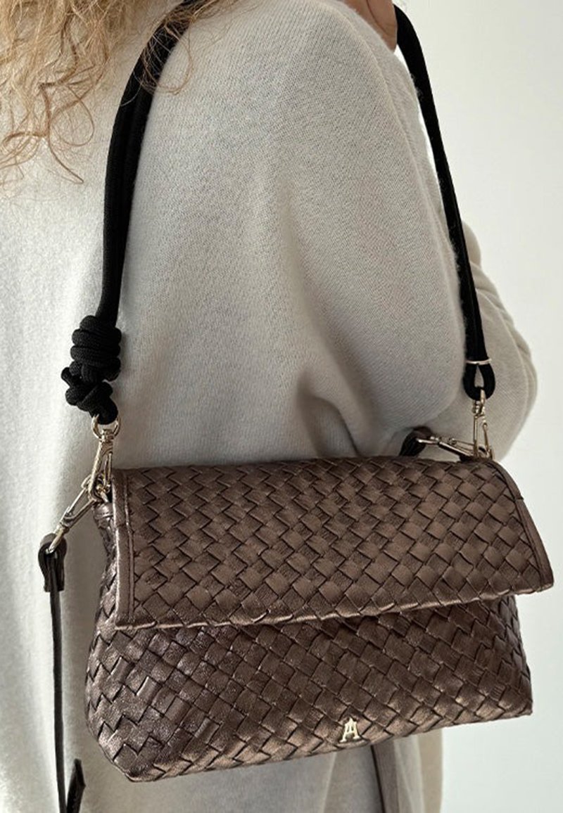 Sac à main en bronze métallique tissé avec un design plié, doté d'une sangle noire tressée et d'accessoires en métal argenté.