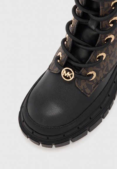 Bottine en cuir noir avec panneau en textile à motifs marron, accents en métal doré, bout rond, semelle en caoutchouc noir épaisse et lacets.