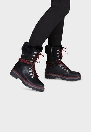 Bottines en cuir noir avec lacets rouges et noirs, col en fausse fourrure, ferrures en argent et semelle robuste. Zippé sur un côté pour un enfilage facile.