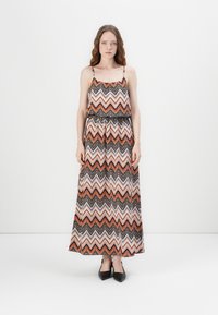 Maxi-jurk met een zigzagpatroon in oranje, zwart en wit. Gemaakt van lichtgewicht stof met dunne schouderbandjes en een elastische taille.