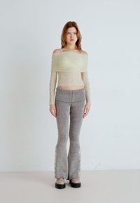 Off-shoulder strikket topp i kremfarge, strukturert stoff; kombinert med ribbede, flerfargede slengbukser med sidelukking. Svarte sko.