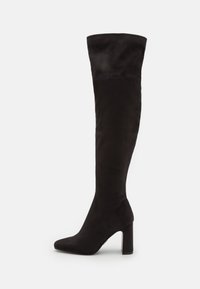 Bottes noires au-dessus du genou en tissu souple, avec un bout pointu et un talon épais, présentant une texture lisse et sans embellissements visibles.