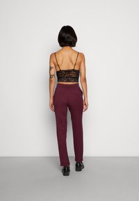 Czarny koronkowy top, burgundowe spodnie dresowe z elastycznym pasem, dwa tylne kieszenie i czarne obuwie. Prezentowane od tyłu.