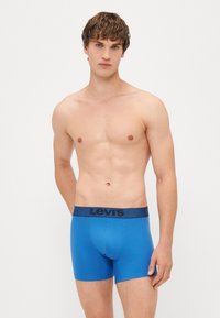 Férfi kék boxer nadrág puha anyagból, sötétkék elasztikus derékpánttal, amelyen a "LEVI'S" logó látható. Ívelt fazon, a comb közepéig ér.