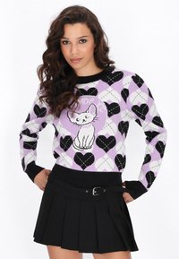 Sweter z dzianiny z wzorem serc w kolorach czarnym, białym i lawendowym, z białym wzorem kota na środku, zestawiony z czarną plisowaną spódnicą.