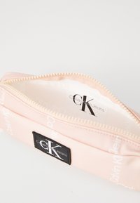 Rosa tygpung med dragkedjeslutning, har "Calvin Klein Jeans"-logotyp på sidan och en mjuk innerfoder.