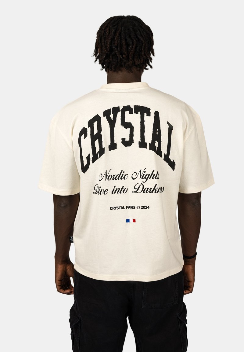 Krémové oversized tričko s výrazným černým textem na zadní straně: "CRYSTAL," "Nordic Nights Dive into Darkness," a malou francouzskou vlajkou.