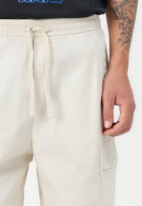 Beiga cargobyxor med elastisk midja och dragsko. Har en sidoficka och en mjuk, lätt tygtextur.