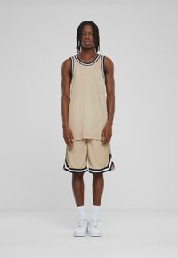 Beige sportstopp med svart og hvitt trim, sammen med matchende shorts som har sidespalter og en teksturert stoff. Hvite sneakers er brukt.