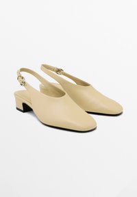 Scarpe slingback beige con punta appuntita, materiale in pelle liscia, tacco a blocco piccolo e cinturino regolabile con fibbia metallica.