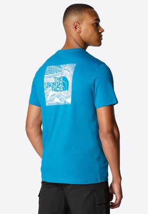 Camiseta de algodón azul de manga corta con un diseño gráfico blanco en la parte posterior, que incluye "The North Face" y motivos abstractos de montañas.