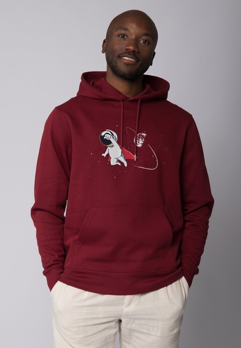 Sweat à capuche bordeaux en tissu doux, orné d'un graphisme d'astronaute au poing serré, entouré d'étoiles. Poche kangourou à l'avant.