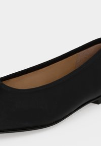 Chaussure de ballet plate noire avec un bout arrondi et une texture cuir lisse, dotée d’une doublure intérieure beige et d’un petit talon.