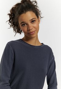 Bluză tricotată cu mânecă lungă, de culoare albastru închis, cu un model texturat, decolteu rotund și croială lejeră, realizată dintr-un material moale și respirabil.