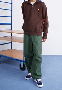 Brązowy bawełniany sweatshirt z kołnierzykiem na pół zamek, z małym logo. Połączony z zielonymi spodniami cargo i granatowymi sneakersami z białymi akcentami.