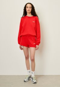 Röd sweatshirt och matchande shorts i fleece-material. Sweatshirten har en liten logotyp, lös passform; shortsen har ett elastiskt midjeband.