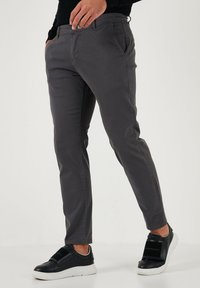 Sive raztegljive chinos hlače s slim fit krojem, ki imajo sprednje žepke in gladko teksturo, v kombinaciji z črnimi športnimi copati.