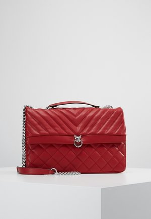 Bolso de mano de cuero acolchado rojo con costuras en forma de chevron y diamante, correa de cadena plateada, asa superior y cierre de anillo plateado sobre superficie blanca.