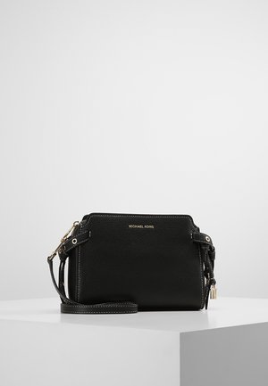 Black leather Michael Kors crossbody bag with gold hardware and adjustable strap, displayed on a white pedestal against a gray background.