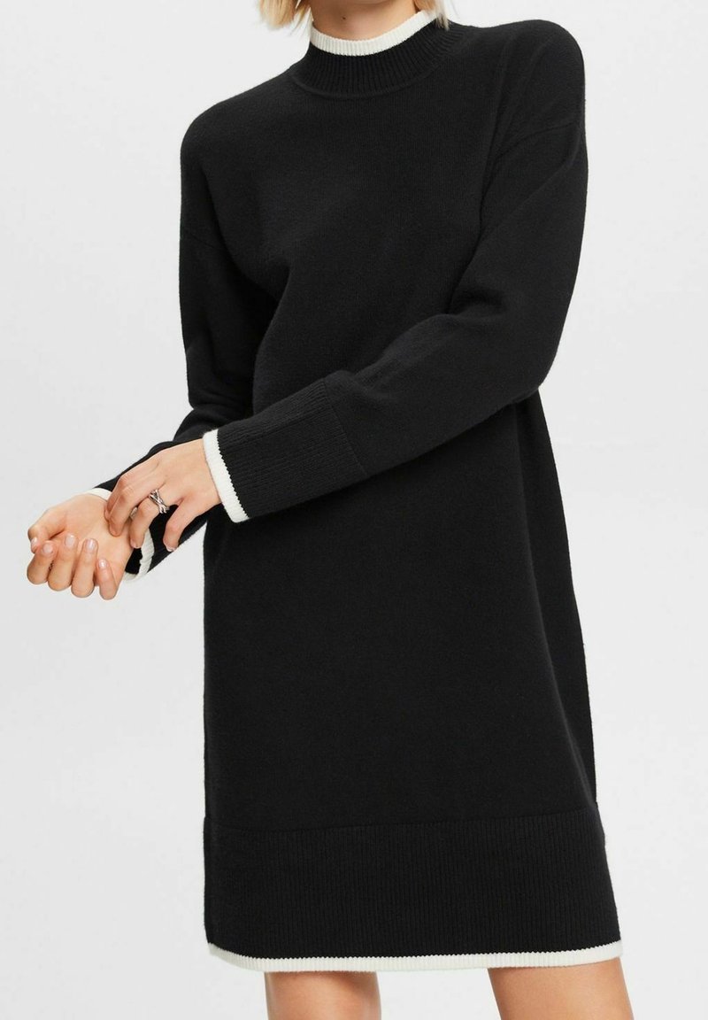 Robe noire en maille avec un col montant, des manches longues et des accents côtelés blancs aux poignets et à l'ourlet. Coupe décontractée, texture douce.