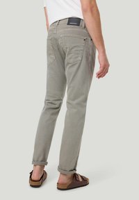 Hellgraue, schmal geschnittene Hose aus weichem Stoff, mit Gesäßtaschen und einem markierten Bund. Aufgerollte Säume an den Knöcheln.