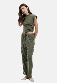 Groen gebreid twee-delig set bestaande uit een cropped top met opgerolde mouwen en losse broek met een verstelbare trekkoord in de taille.