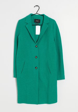 Long manteau vert en laine avec trois boutons marron, col à revers, poches latérales, suspendu sur un cintre noir sur fond blanc.