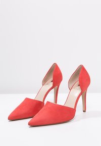 Chaussures à talons hauts en suede rouge avec un bout pointu et un design ouvert à l'arrière, présentant un talon aiguille fin et une doublure intérieure lisse.